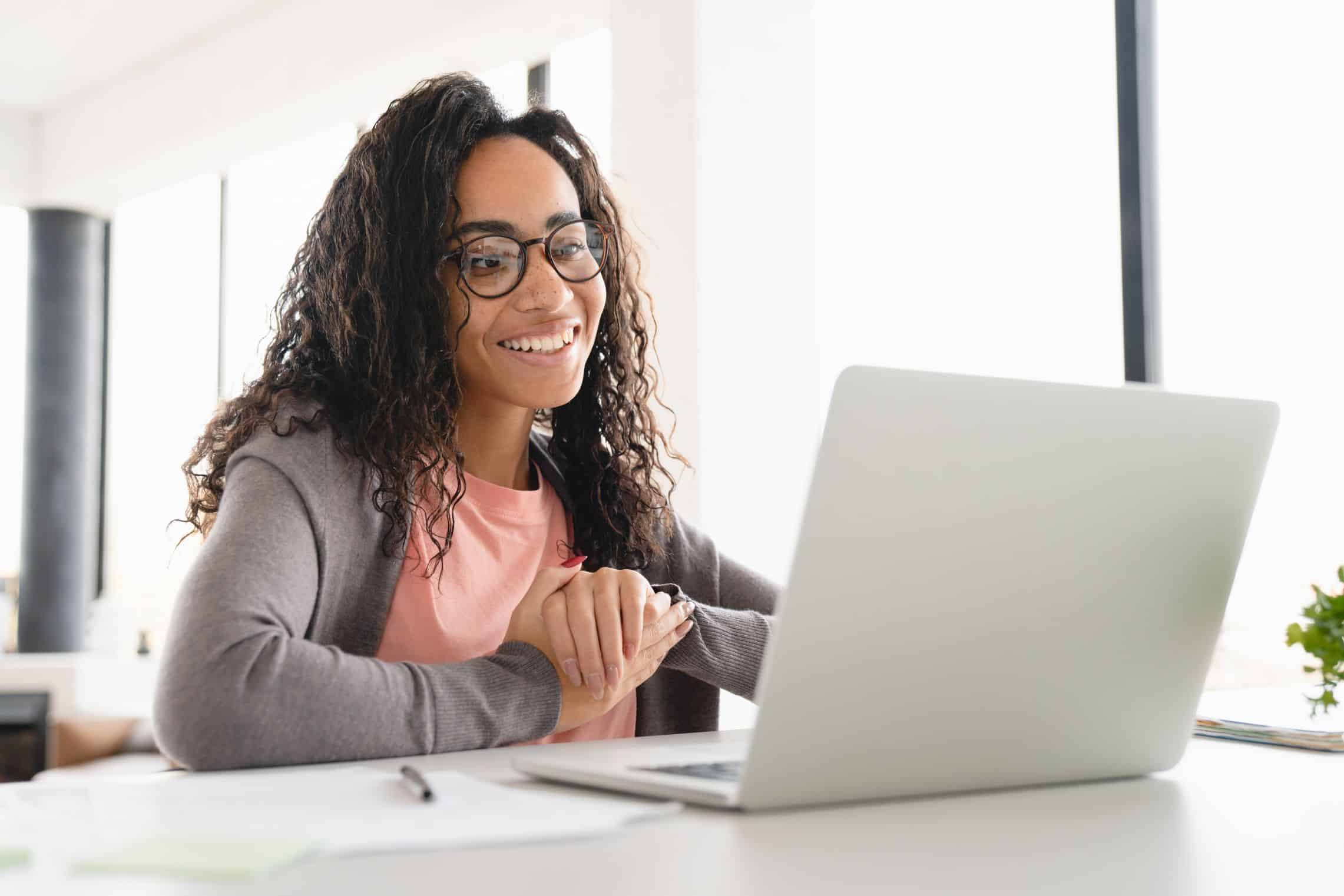 Photo d'une jeune femme souriante devant son ordinateur, se renseigne sur les mentions obligatoires sur une facture électronique 2026